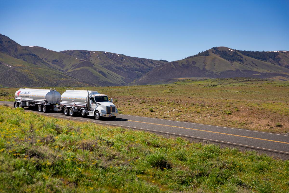 A truck driving through a scenic valley with Cougar Den logo on the side of the tank. 